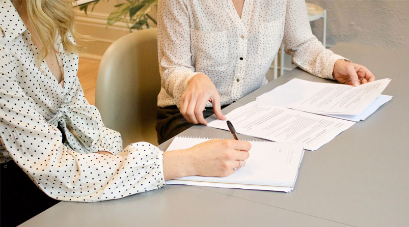 two women completing forms at desk polka dot shirt