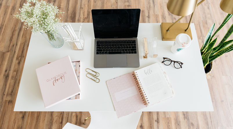 Laptop on white desk with books and glasses