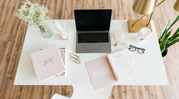 Laptop on white desk with books and glasses